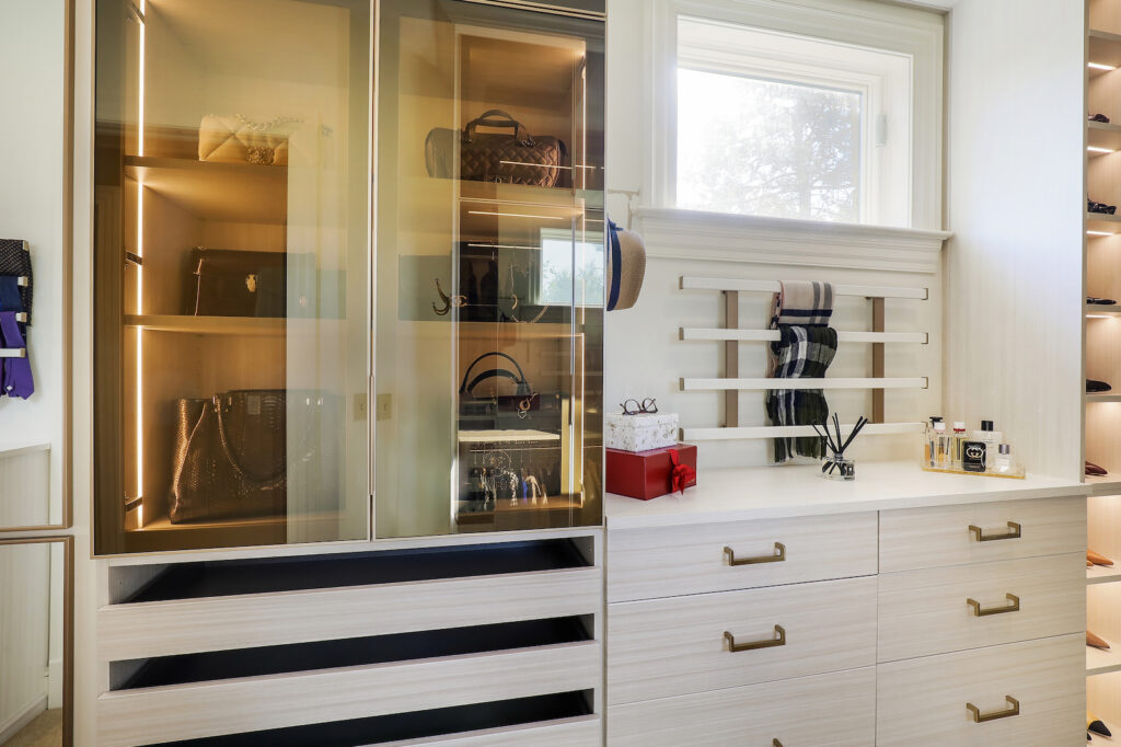 Glass-front closet cabinetry with illuminated shelves and dedicated storage for handbags, accessories, and folded items