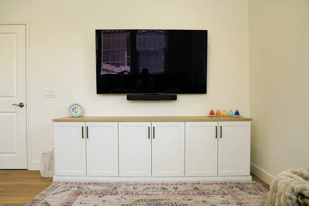 White cabinet with paneled doors and a wood-toned top beneath a wall-mounted television